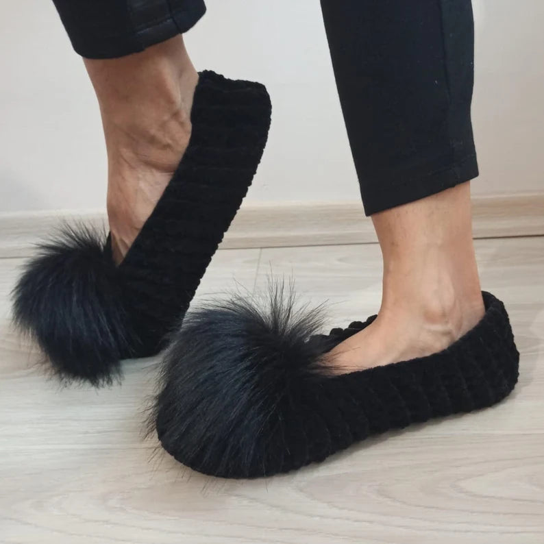 Black fluffy slippers worn indoors on a light wooden floor.