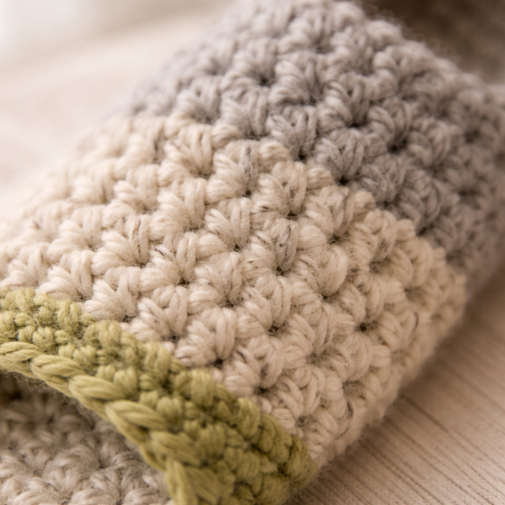 Close-up of a crocheted blanket with a green border on a neutral background