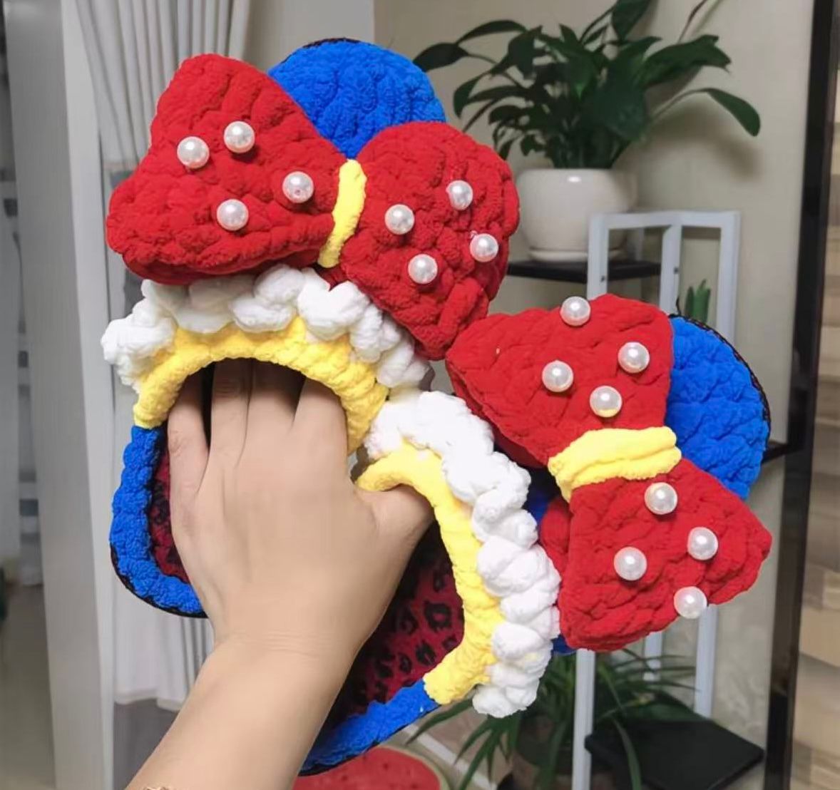 Hand holding a colorful bow-shaped object with pearls in a home setting.
