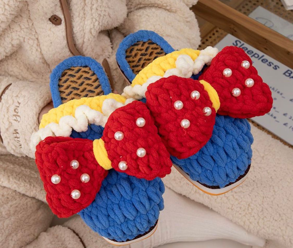 Colorful slippers with red bows and pearls on a textured surface
