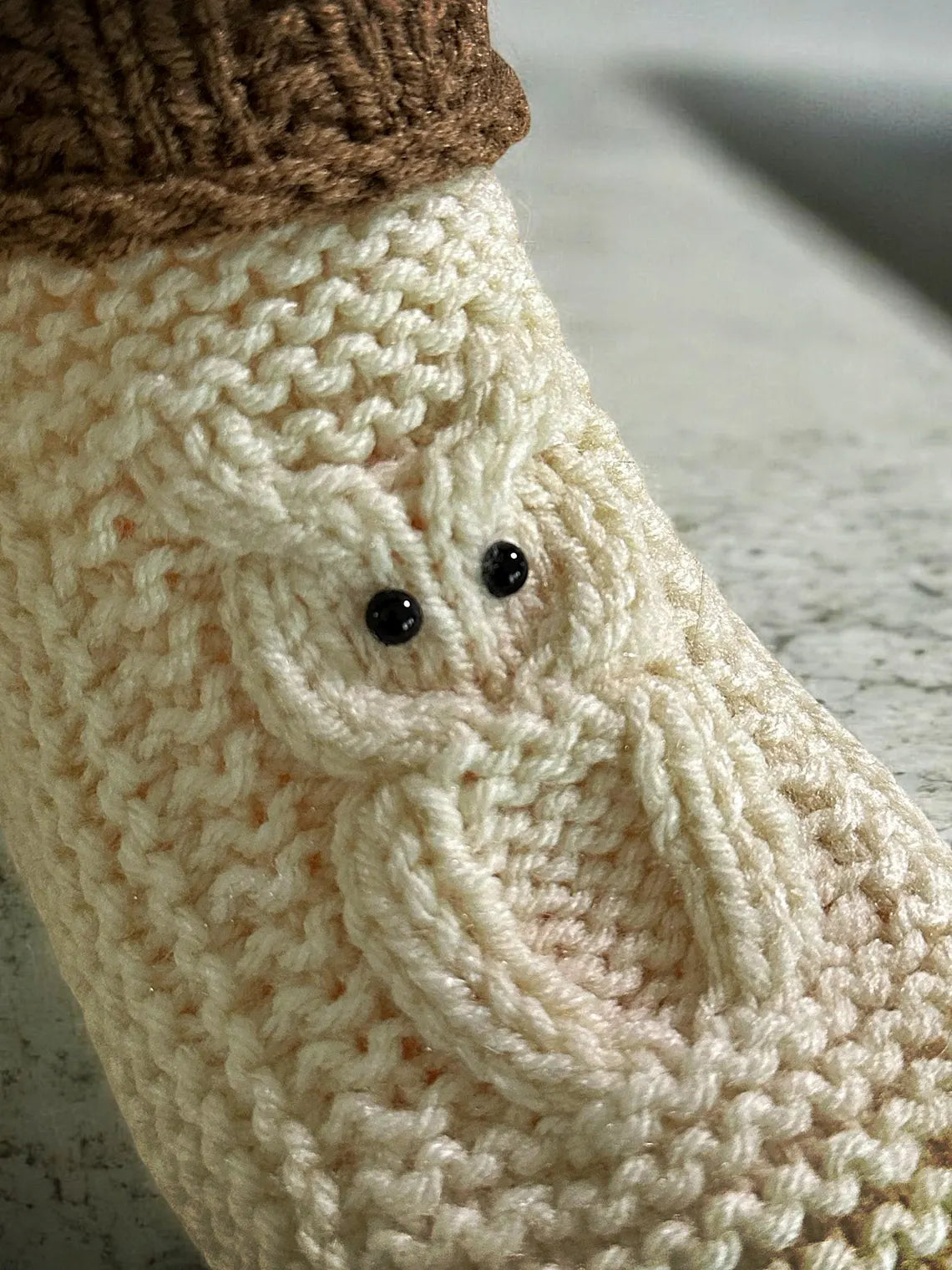 Close-up of a knitted white sock with a small black eye detail on a neutral background