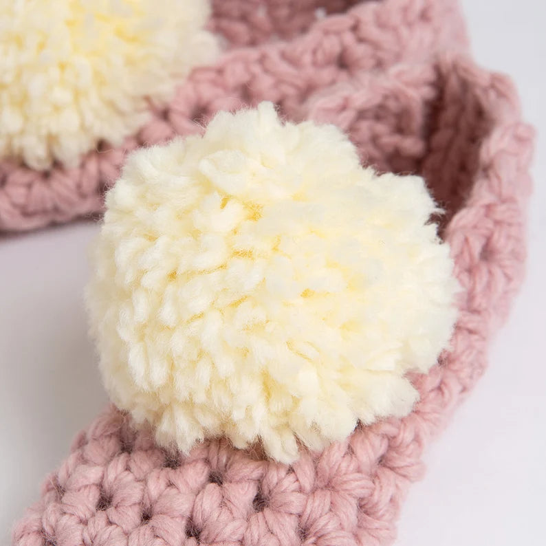 Pink knitted headband with a white pom-pom on a white background