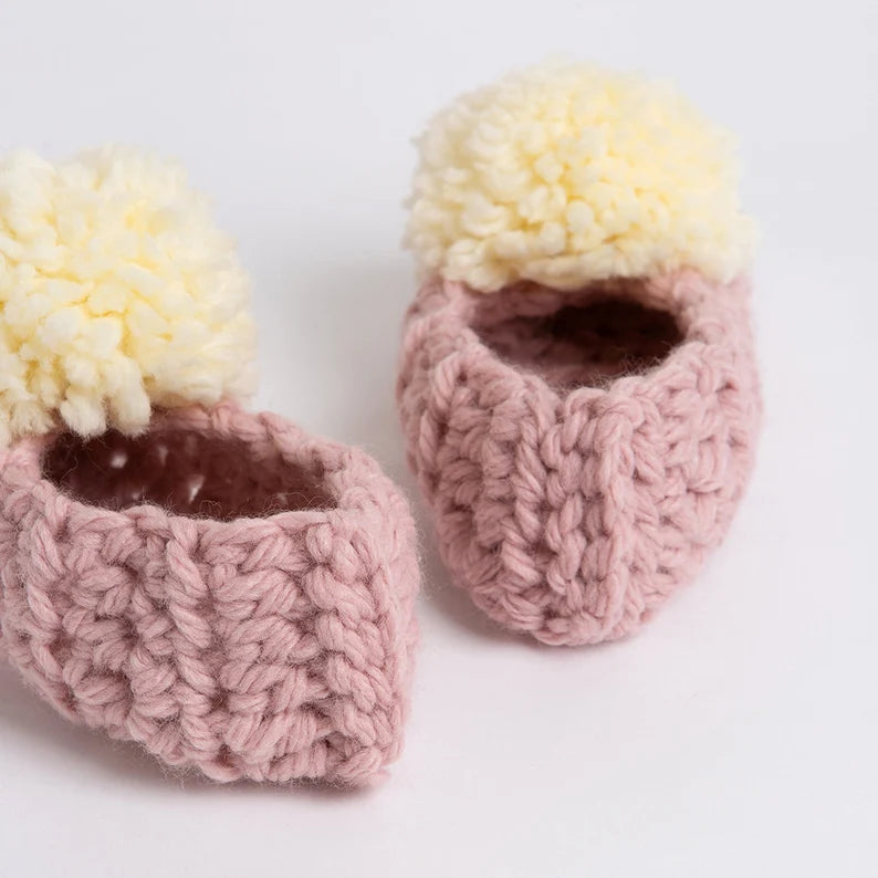 Pair of pink knitted baby booties with yellow pom-poms on a white background