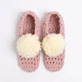 Pair of pink crochet slippers with white pom-poms on a light gray background